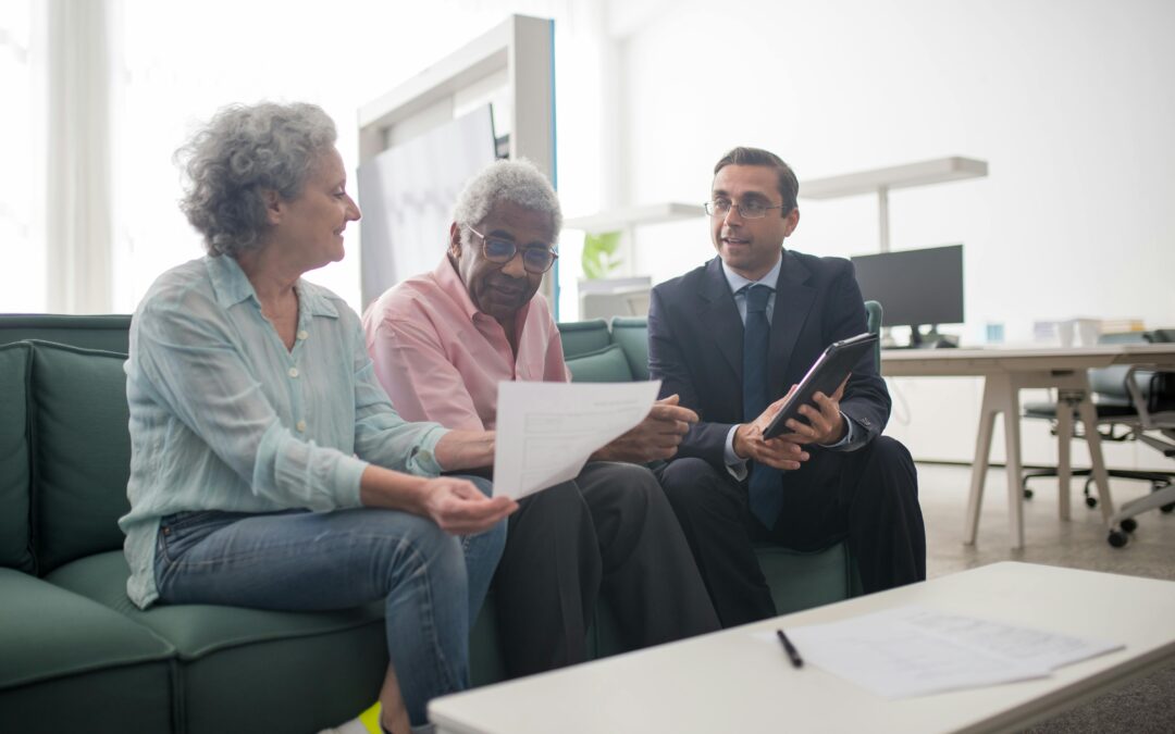 An elderly couple sits on a couch reviewing paperwork while a man sits next to them, showing additional documents related to reverse mortgages and taxes